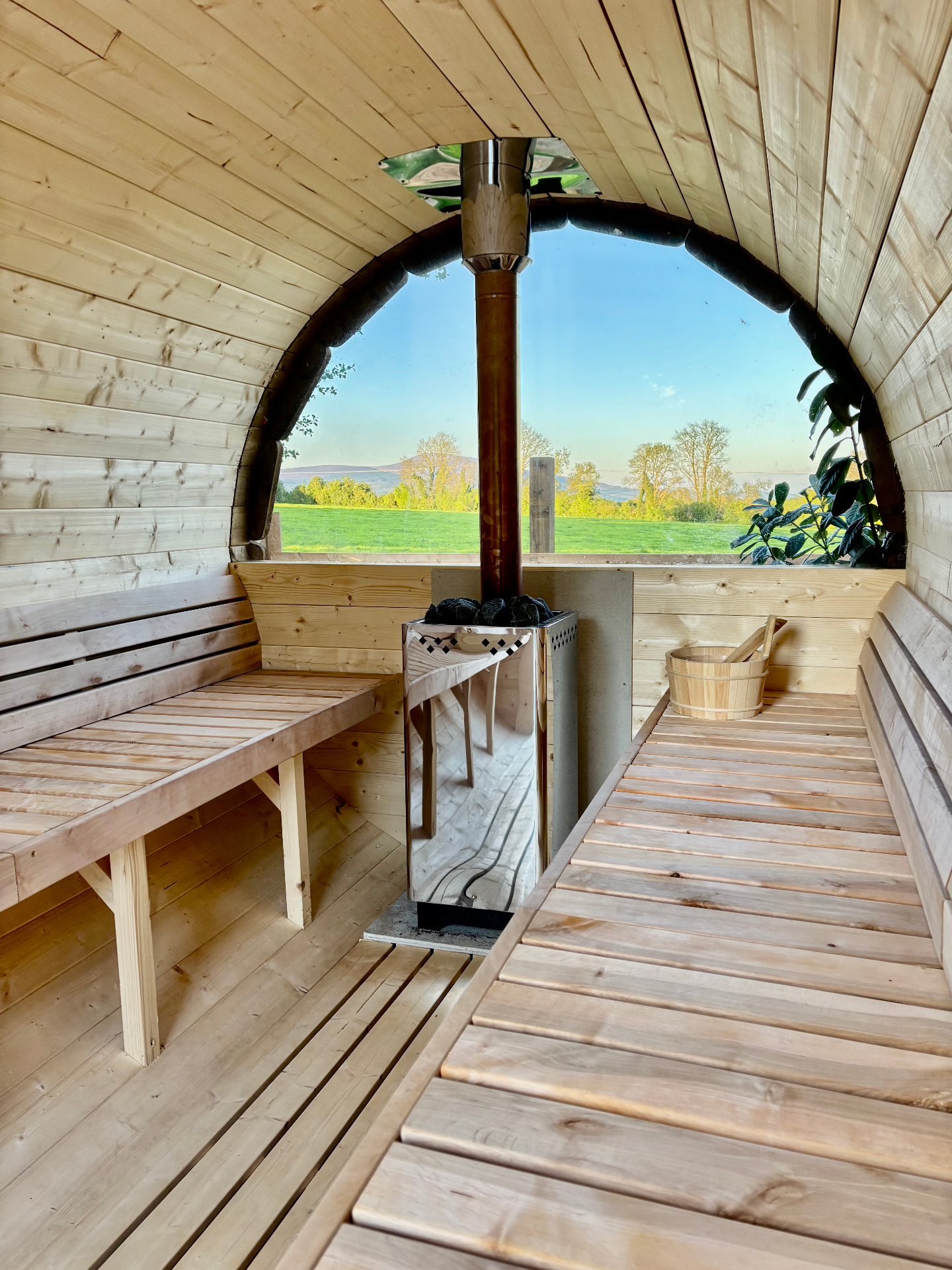 Inside the cedar barrel sauna with wood stove and countryside view